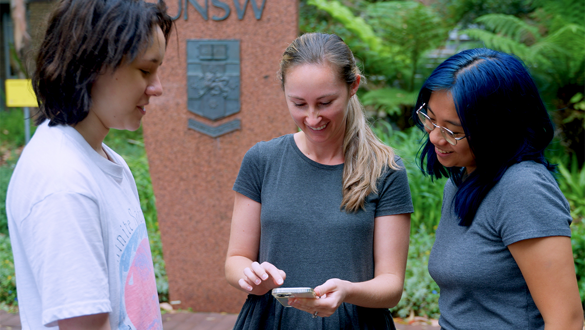 Three people looking down at a mobile phone