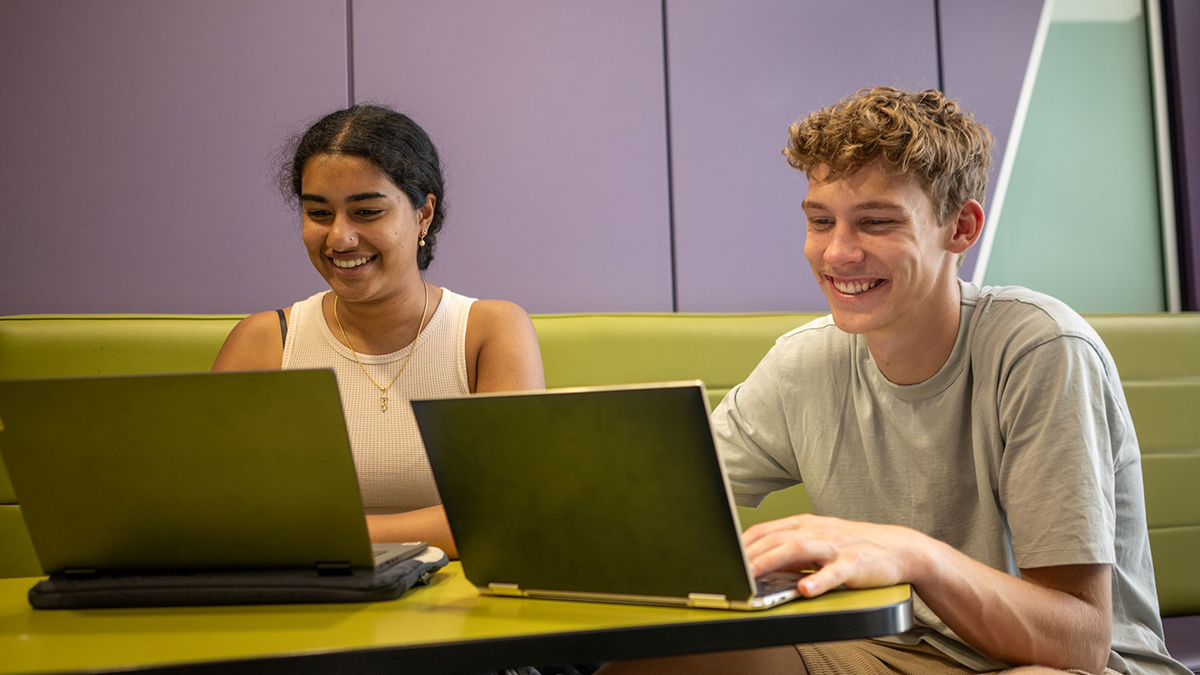 Two students working on laptops and smiling