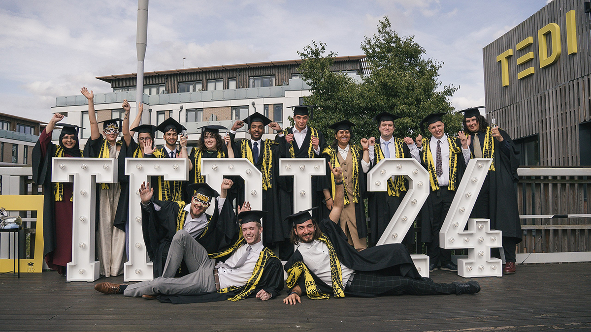 TEDI-London graduates in their graduation robes with a sign that says "TEDI24"