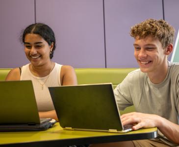 Two students working on laptops and smiling