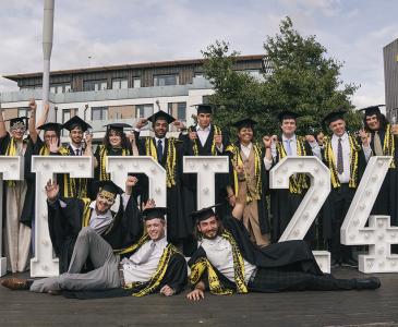 TEDI-London graduates in their graduation robes with a sign that says "TEDI24"